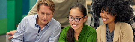 Group of happy multiracial business people sitting at desk in the modern coworking space, looking at laptop screen and smiling, working togetherの写真素材