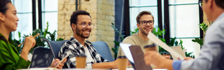 Sharing fresh ideas. Group of young multiracial people sitting at the table in coworking space and working on project together, talking and discussing somethingの写真素材