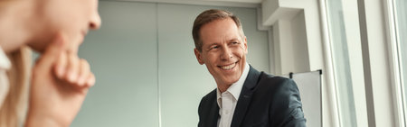 Staff meeting. Handsome mature man in formal wear talking with colleagues and smiling while sitting in the officeの写真素材