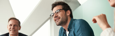 Happy to work here Young and handsome man in eyeglasses discussing something with colleagues and smiling while sitting in the modern officeの写真素材