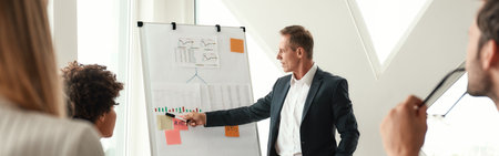Analyzing results. Mature businessman standing near whiteboard and explaining something to his colleaguesの写真素材
