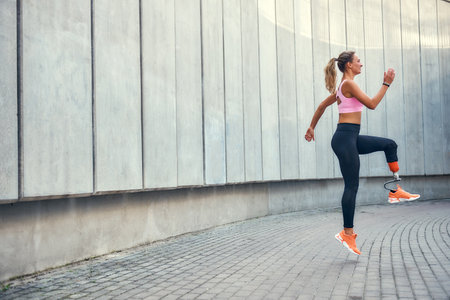 No limits Active disabled woman with leg prosthesis in sports clothing jumping while her morning workout outdoors. Disabled sport conceptの写真素材