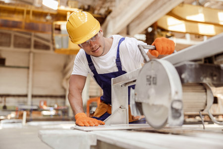 Smiling male worker using sawing machine in workshopの写真素材