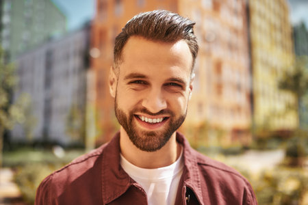 Hello Portrait of happy attractive man with stubble smiling and looking at camera while standing on the streetの写真素材