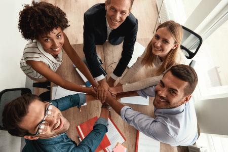 Top view of business people holding hands together and looking at camera with smile while sitting in the officeの写真素材