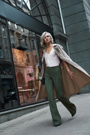 Fashion. Young stylish woman walking on the city street looking aside curious full body shotの写真素材