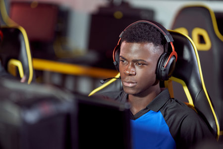 Portrait of focused african cybersport male gamer wearing headphones playing video games, participating in eSport tournamentの写真素材