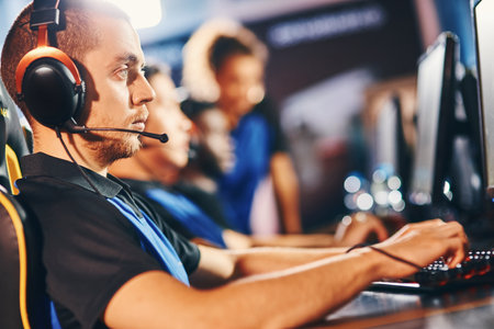Cybersport gamer. Side view of a young fully concentrated guy wearing headphones playing online video gamesの写真素材