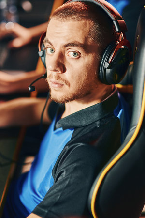 Portrait of a young caucasian guy wearing headphones looking at camera while participating in eSport tournament, sitting in gaming club or internet cafeの写真素材