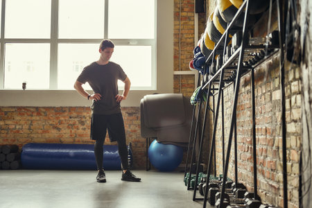 Ready for workout. Confident young man is looking at sport equipment while exercising at gym.の写真素材