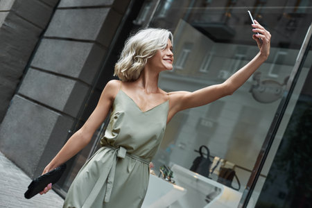 Fashion. Young stylish woman walking on the city street taking selfie photo on smartphone smiling cheerfulの写真素材