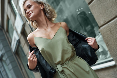Fashion. Young stylish woman walking on the city street taking off jeans jacket smiling joyful close-upの写真素材