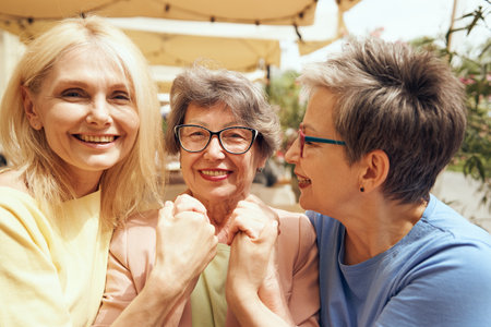Happy middle age women are hugging and look at camera while sitting in cafe. Female friendshipの写真素材