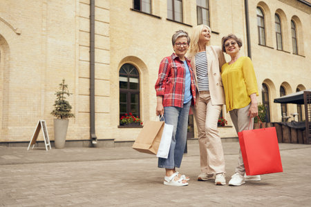 Smiling stylish senior women standing outdoors with shopping bags in the city centre. Seasonal salesの写真素材