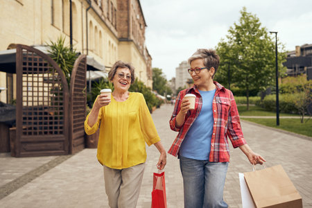 Smiling stylish senior women meeting outdoors, drinking coffee and shopping in the city centreの写真素材