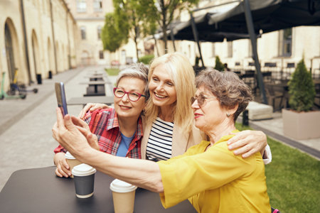 Mature smiling women friends taking selfie on phone while sitting in cafe terraceの写真素材