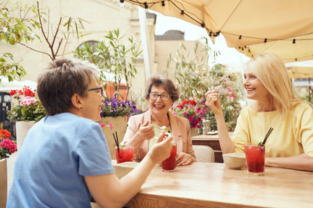 Mature female friends sitting in cafe, drinking cocktails and laughing while enjoying a lunch dateの写真素材