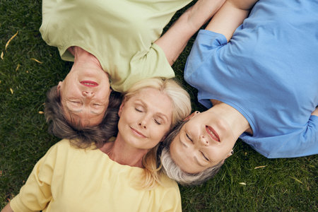 Top view of smiling mature women friends lying head to head on grass and with closed eyesの写真素材