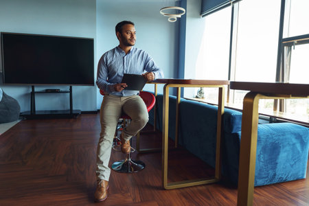 Handsome businessman sitting desk in coworking with clipboard and looking at sideの写真素材