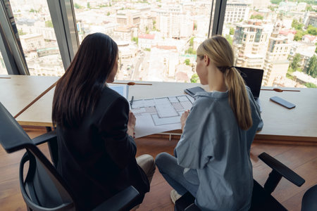 Back view of two female design engineer working with project documents sitting in office near windowの写真素材