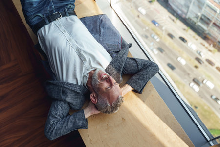Top view of tired senior businessman resting on wooden banch in office during break timeの写真素材