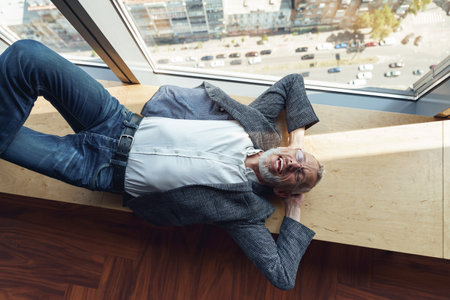 Top view of tired smiling senior businessman resting on wooden banch in office during break timeの写真素材