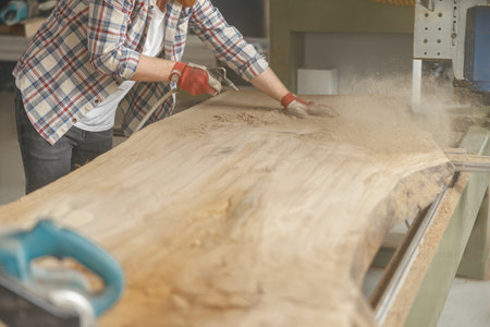 Close up of carpenter is cleaning saw from sawdust with air compressor working in carpentry workshopの写真素材