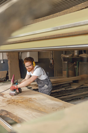 Bearded male wood worker using electric sander for wood. Carpentry workshop. High quality photoの写真素材