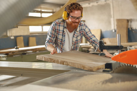 Male carpenter sawing a board with a circular saw in a carpentry workshop. High quality photoの写真素材