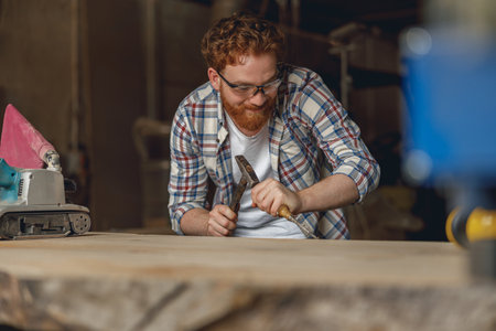 Close up of craftsman working with chisel while cutting wooden plank in carpentry workshop