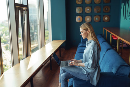 Smiling woman manager working on laptop with documents sitting in cozy office during working dayの写真素材