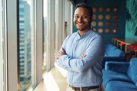 Smiling entrepreneur with crossed arms standing in office near window and looking at cameraの写真素材