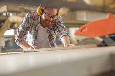 Smiling carpenter cutting wooden board at sawmill carpentry manufacturing . Sawing machineの写真素材