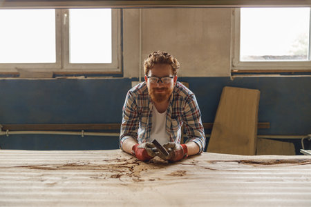 Craftsman working with chisel while cutting wooden plank in carpentry workshop and looks cameraの写真素材