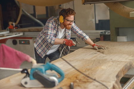 Woodworker is cleaning saw from sawdust working in carpentry workshop. High quality photoの写真素材