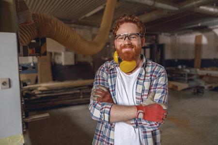 Smiling woodworker with crossed hands standing on the background on carpentry workshopの写真素材