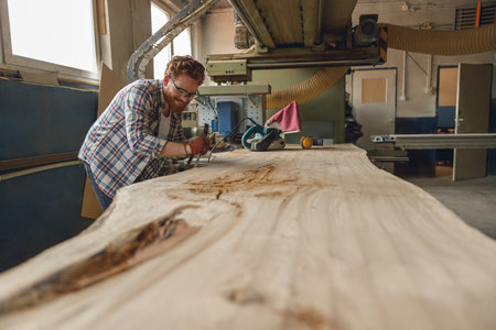 Professional craftsman working with chisel while cutting wooden plank in carpentry workshopの写真素材