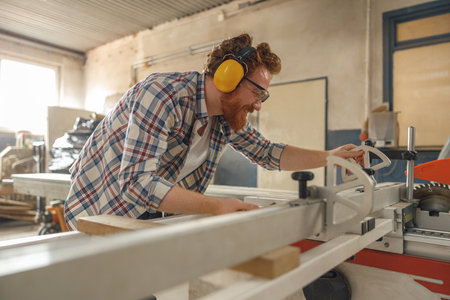 Male carpenter sawing a board with a circular saw in a carpentry workshop. High quality photoの写真素材