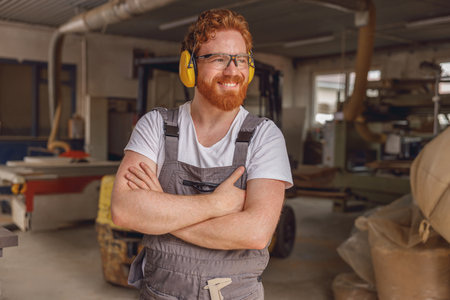 Smiling woodworker with crossed hands standing on the background on carpentry workshopの写真素材