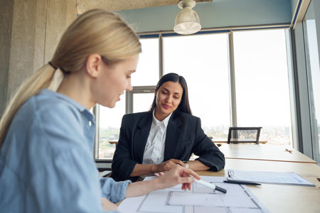 Close up of two female design engineer working with project documents sitting in office near windowの写真素材