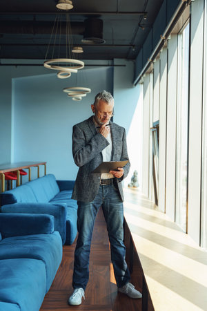 Focused businessman looking on documents and think how to solve problem while standing in officeの写真素材