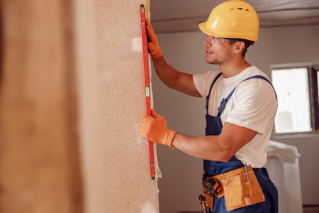 Joyful male builder measuring wall in houseの写真素材