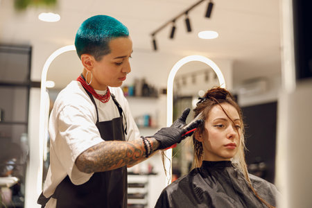 Colorist dyes hair of woman with brush and foil in beauty salon. Professional hair care productsの写真素材
