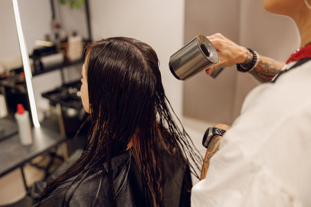 Back view of professional female barber with hair dryer styling hair of customer in salon