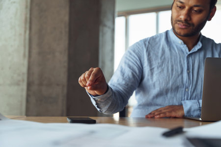 A man is seated at a table with a laptop and scattered papersの写真素材