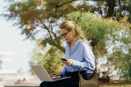 A Professional Woman Engaged in Work While Embracing the Beauty of Nature with Her Laptop and Phoneの写真素材