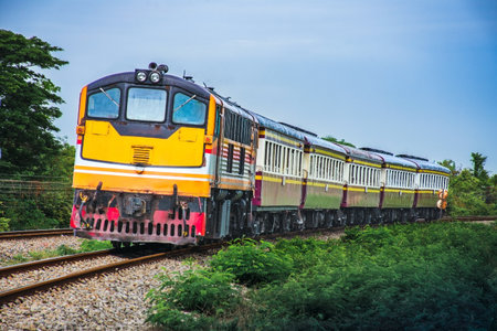 Passenger train by diesel locomotive on the railway curve in Thailand on the background of blue sky.の写真素材