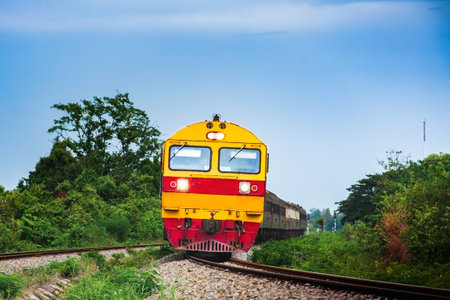 Passenger train by diesel locomotive on the railway curve in Thailand on the background of blue sky.の写真素材