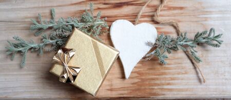 Photo of golden gift with white heart on wooden background and plantの写真素材
