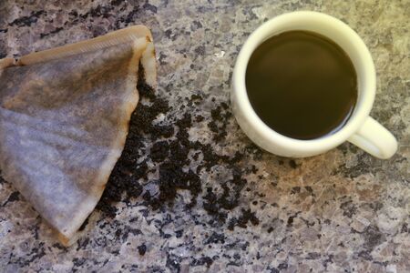 table with coffee grounds in the strainer and white cup with coffee